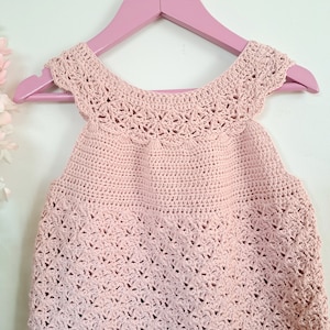 Peut inclure: Un haut crocheté rose sans manches avec une délicate bordure en dentelle autour du cou et des épaules.