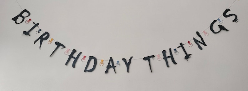 May include: A black and white banner with the words "Birthday Things" strung with colorful lightbulbs.