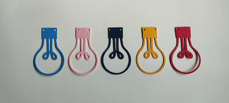 May include: Six lightbulb shaped cutouts in different colors: blue, pink, navy blue, yellow, and red. The cutouts are made of felt and have a simple design.