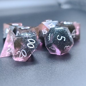 May include: A set of six pink and black dice with white numbers. The dice are made of a translucent material with a glittery finish.