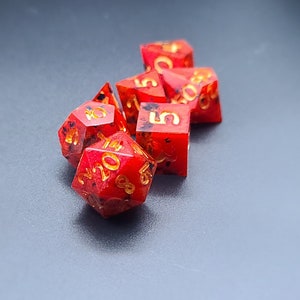 May include: A set of six red and gold dice with black flecks. The dice are in various shapes and sizes, with numbers 2, 3, 4, 5, and 6 visible.