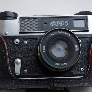 May include: A black and silver 35mm film camera with a leather case. The camera has a lens labeled "INDUSTAR-61/L/D" and a top plate that reads "ФЭД 5".