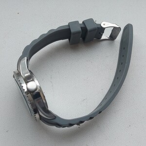 May include: A silver watch with a gray rubber strap. The watch has a round face and a silver bezel.