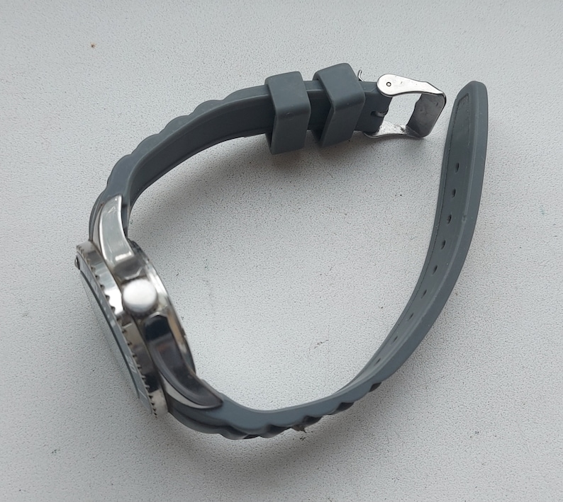 May include: A silver watch with a gray rubber strap. The watch has a round face and a silver bezel.