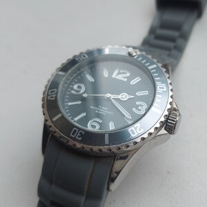 May include: A silver and black wristwatch with a blue face and white markings. The watch has a black rubber band and says "10 BAR WATER RESISTANT QUARTZ" on the face.