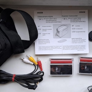 Peut inclure: Une caméra vidéo numérique Samsung noire avec un étui de transport noir, deux cassettes vidéo, un adaptateur secteur et un jeu de câbles AV. La caméra dispose d'un zoom numérique et d'un microphone intégré.