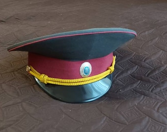 May include: A black and red military style hat with a gold braid and a blue and silver emblem.