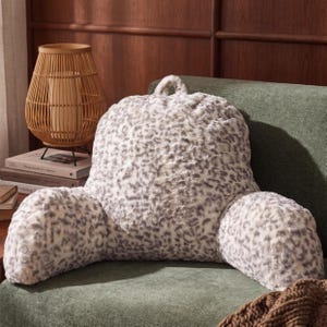 May include: A plush reading pillow featuring a white and gray leopard print pattern. The pillow has a high backrest with two integrated armrests on the sides and a small fabric loop handle at the top center for easy carrying and positioning.
