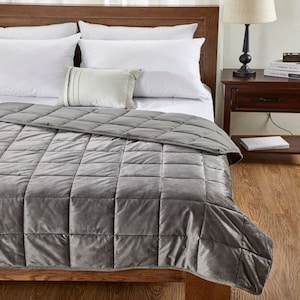 May include: A gray weighted blanket with a quilted design. The blanket is folded on a bed with white pillows and a decorative pillow.