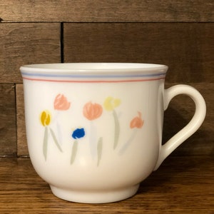 May include: White ceramic mug with a blue, pink, and red rim. The mug has a floral design with yellow, orange, pink, and blue flowers.