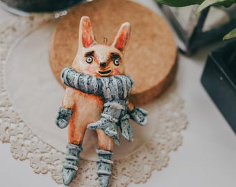 Puede incluir: Una figurita artesanal caprichosa de una criatura con un hocico largo, ojos grandes y una bufanda azul. La figurita está hecha de arcilla pintada y tiene una superficie texturizada.