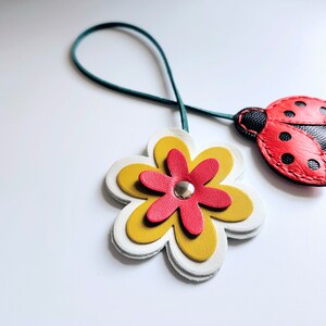 May include: A green leather cord with a red and black ladybug charm and a white, yellow, and red flower charm.