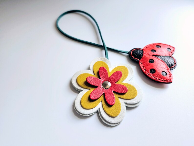 May include: A green leather cord with a red and black ladybug charm and a white, yellow, and red flower charm.
