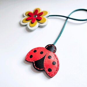 May include: A red and black ladybug with black dots and a green leather strap attached to a yellow and white flower with a red center.