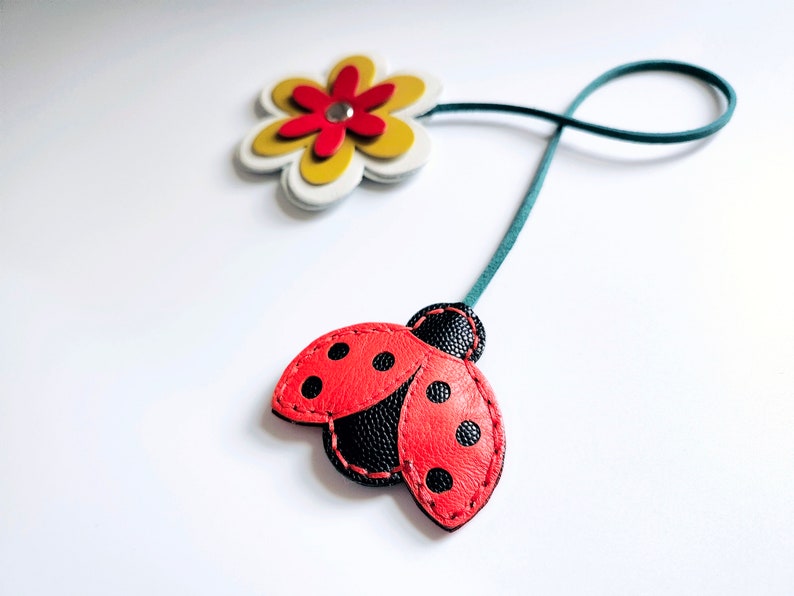 May include: A red and black ladybug with black dots and a green leather strap attached to a yellow and white flower with a red center.