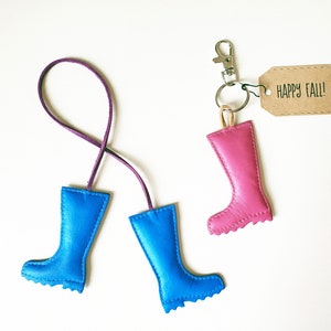 May include: A collection of leather boot keychains in blue and pink, with a purple cord and a silver clasp. One keychain has a tag that says "HAPPY FALL!"