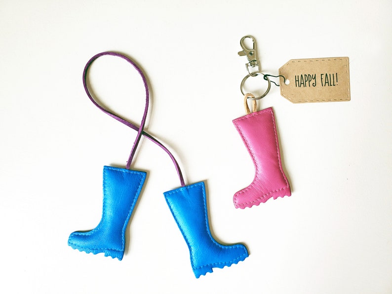 May include: A collection of leather boot keychains in blue and pink, with a purple cord and a silver clasp. One keychain has a tag that says "HAPPY FALL!"