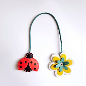 May include: A green leather bookmark with a red ladybug and a yellow flower with a green center.