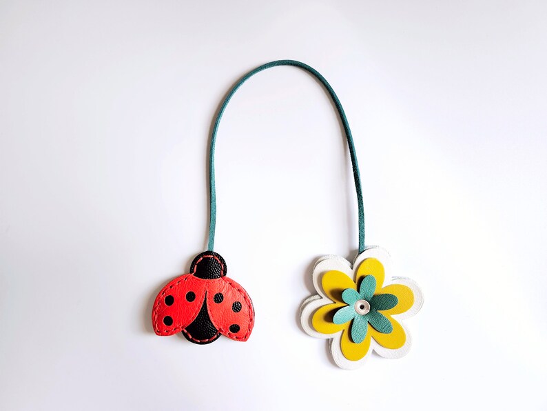 May include: A green leather bookmark with a red ladybug and a yellow flower with a green center.