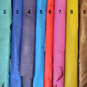 May include: A collection of ten rolls of leather in various colors. The colors include shades of turquoise, blue, purple, red, pink, yellow, brown, and white. The leather appears to be smooth and has a slight sheen.