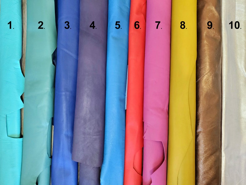 May include: A collection of ten rolls of leather in various colors. The colors include shades of turquoise, blue, purple, red, pink, yellow, brown, and white. The leather appears to be smooth and has a slight sheen.