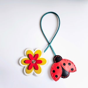 Leather bag charm with a red and black ladybug and a yellow and red flower. The ladybug has black dots on its wings and the flower has a white center.