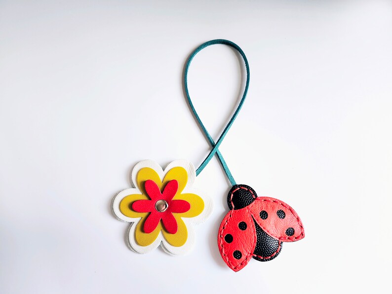 Leather bag charm with a red and black ladybug and a yellow and red flower. The ladybug has black dots on its wings and the flower has a white center.