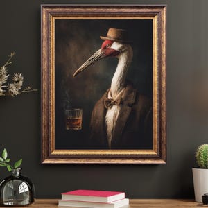 May include: Framed artwork featuring a crane in a brown suit, bow tie, and hat, holding a glass of whiskey. The bird has a white neck, red markings, and a long beak. The frame is ornate with a gold finish.