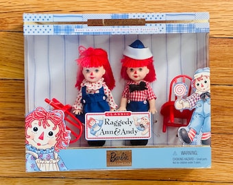 Puede incluir: Un set de Barbie Collector Edition con muñecas Raggedy Ann & Andy. Las muñecas tienen cabello de hilo rojo, caras pintadas y visten trajes de estilo vintage. El set incluye una silla roja y un letrero que dice "Raggedy Ann & Andy".