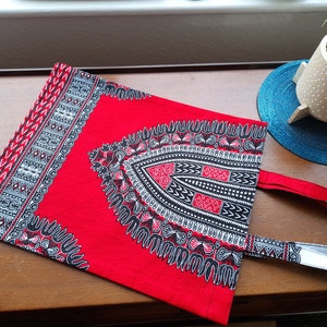 May include: Red tote bag with a black and white geometric pattern. The bag has a single strap and is made of fabric.