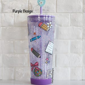 Puede incluir: Vaso de purpurina morado con tapa transparente y una pajita. El vaso tiene una variedad de pegatinas con tem&aacute;tica escolar, incluyendo un l&aacute;piz, un cray&oacute;n, una regla, un cuaderno y un lazo. El texto "DaisyMoonDesigns" es visible en el vaso.
