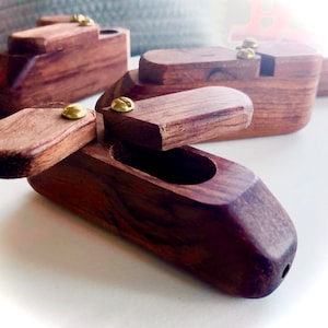 May include: Several small, wooden boxes with hinged lids and brass screws. The boxes are a rich, dark brown color with visible wood grain. One box has its lid open, revealing an interior cavity. The boxes appear to be handmade.