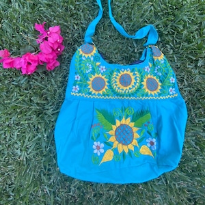 May include: A turquoise blue shoulder bag with a long strap. The bag is embroidered with yellow sunflowers and green leaves.