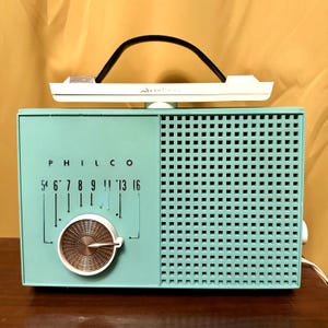 May include: A vintage turquoise blue Philco radio with a white dial and a black knob. The radio has a grid pattern on the front and the text "PHILCO" and "5 6 7 8 9 11 13 16" printed on the front.