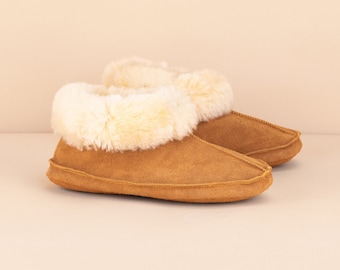 Pode incluir: Um par de pantufas de camurça marrom com uma borda de pele sintética branca. As pantufas são macias e aconchegantes, perfeitas para manter os pés aquecidos no inverno.