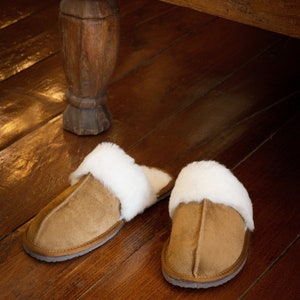 May include: Two pairs of brown suede slippers with white faux fur lining. The slippers are on a wooden floor.