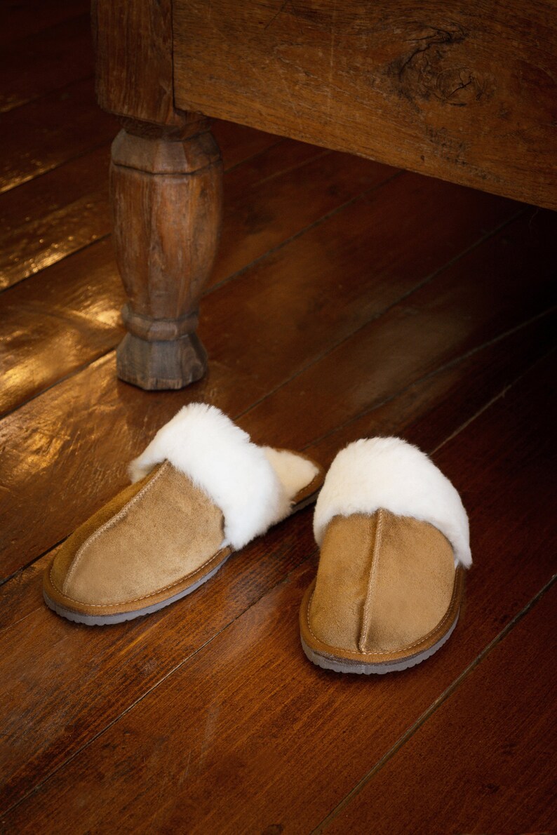 May include: Two pairs of brown suede slippers with white faux fur lining. The slippers are on a wooden floor.