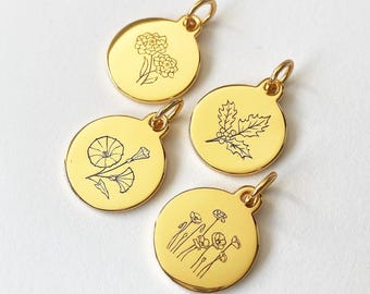 May include: Four gold-coloured round pendants with black etched floral designs. The pendants feature different botanical illustrations, including flowers and leaves. Each pendant has a small loop at the top for attaching to a chain or bracelet.