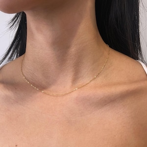 May include: A delicate gold chain necklace featuring thin, interlocking links worn around the neck, paired with a single drop earring consisting of a small gold stud attached to a smooth, white, teardrop-shaped pearl that hangs from the earlobe.