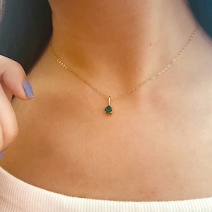 Op de afbeelding: Een delicate gouden ketting met een kleine, vierkant geslepen, donkergroene edelsteen hanger. De hanger hangt aan een fijne gouden ketting, wat een minimalistisch en elegant ontwerp creëert. De ketting wordt om de nek gedragen.