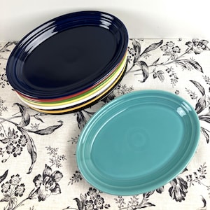 May include: A stack of oval serving platters in various colors, including navy blue, red, yellow, and white. A single turquoise oval platter is in the foreground.