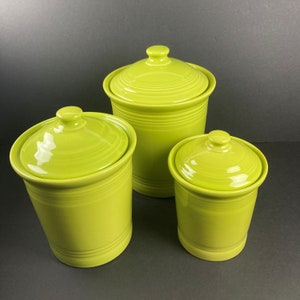 May include: Three lime green ceramic canisters with lids. The canisters are different sizes and have a glossy finish.