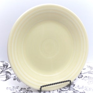 May include: A large, cream-colored ceramic dinner plate with a slightly rippled edge. The plate has a smooth, glossy finish.