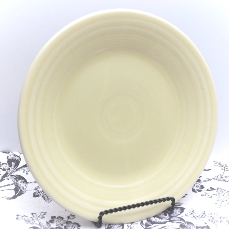 May include: A large, cream-colored ceramic dinner plate with a slightly rippled edge. The plate has a smooth, glossy finish.