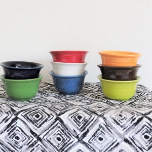 May include: A collection of eight ceramic bowls arranged in three stacks. The bowls feature a glossy finish and come in various solid colors including dark blue, light green, red, white, medium blue, orange, dark brown, and lime green.