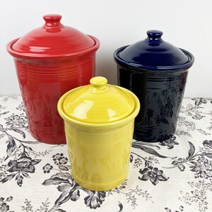 May include: Set of three ceramic canisters with lids in red, yellow, and blue. The canisters are all the same style with a ribbed design.
