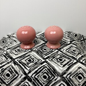 May include: A set of two pink ceramic salt and pepper shakers. The shakers are round with a small opening on top for dispensing salt and pepper. They have a smooth, glossy finish.