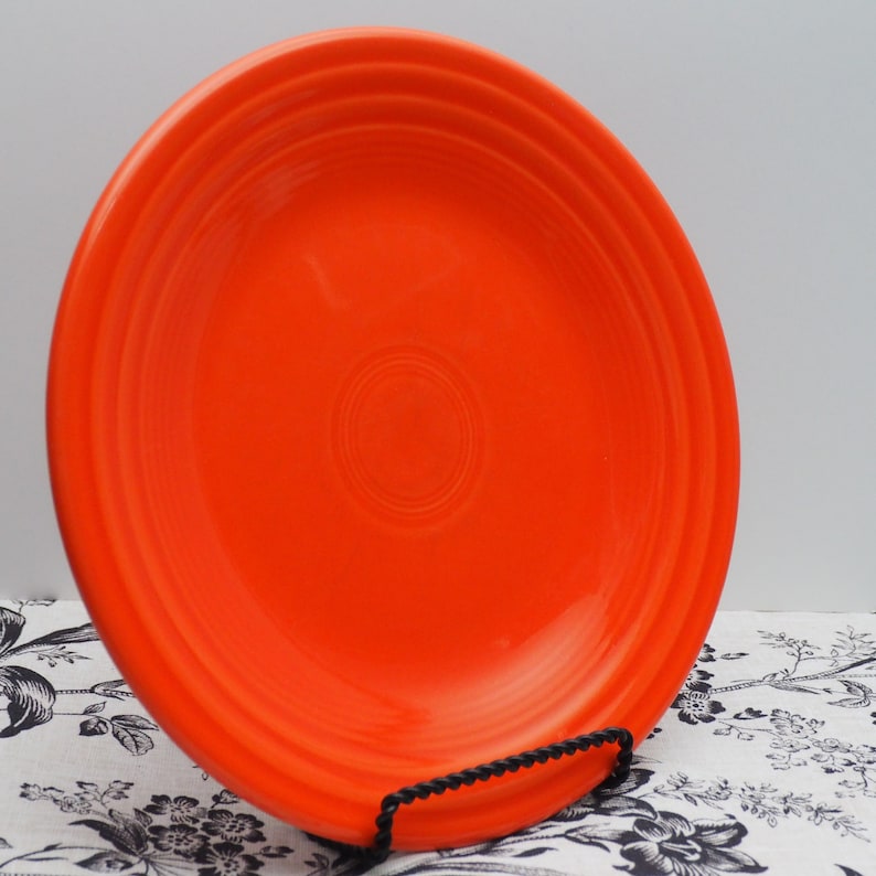 May include: A bright orange ceramic dinner plate with a slightly raised rim and a subtle concentric circle design in the center.
