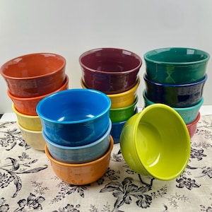 May include: A stack of colorful ceramic bowls in various shades of red, orange, yellow, green, blue, and purple. The bowls are arranged in a pyramid shape, with the largest bowl at the bottom and the smallest bowl at the top.