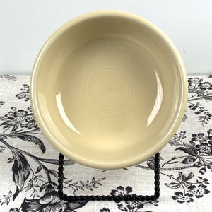 Peut inclure: Un bol rond en c&eacute;ramique de couleur cr&egrave;me avec une finition lisse et brillante et un bord large l&eacute;g&egrave;rement sur&eacute;lev&eacute;. L'int&eacute;rieur du bol pr&eacute;sente un motif circulaire concentrique subtil centr&eacute; &agrave; la base, refl&eacute;tant la lumi&egrave;re sur ses parois.